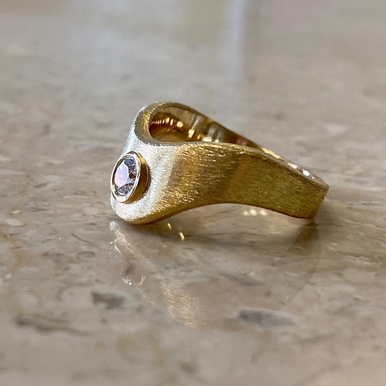 18 karat bred guldring i organisk bølgeform, ridset overflade, med stor 0,30ct hvid diamant.