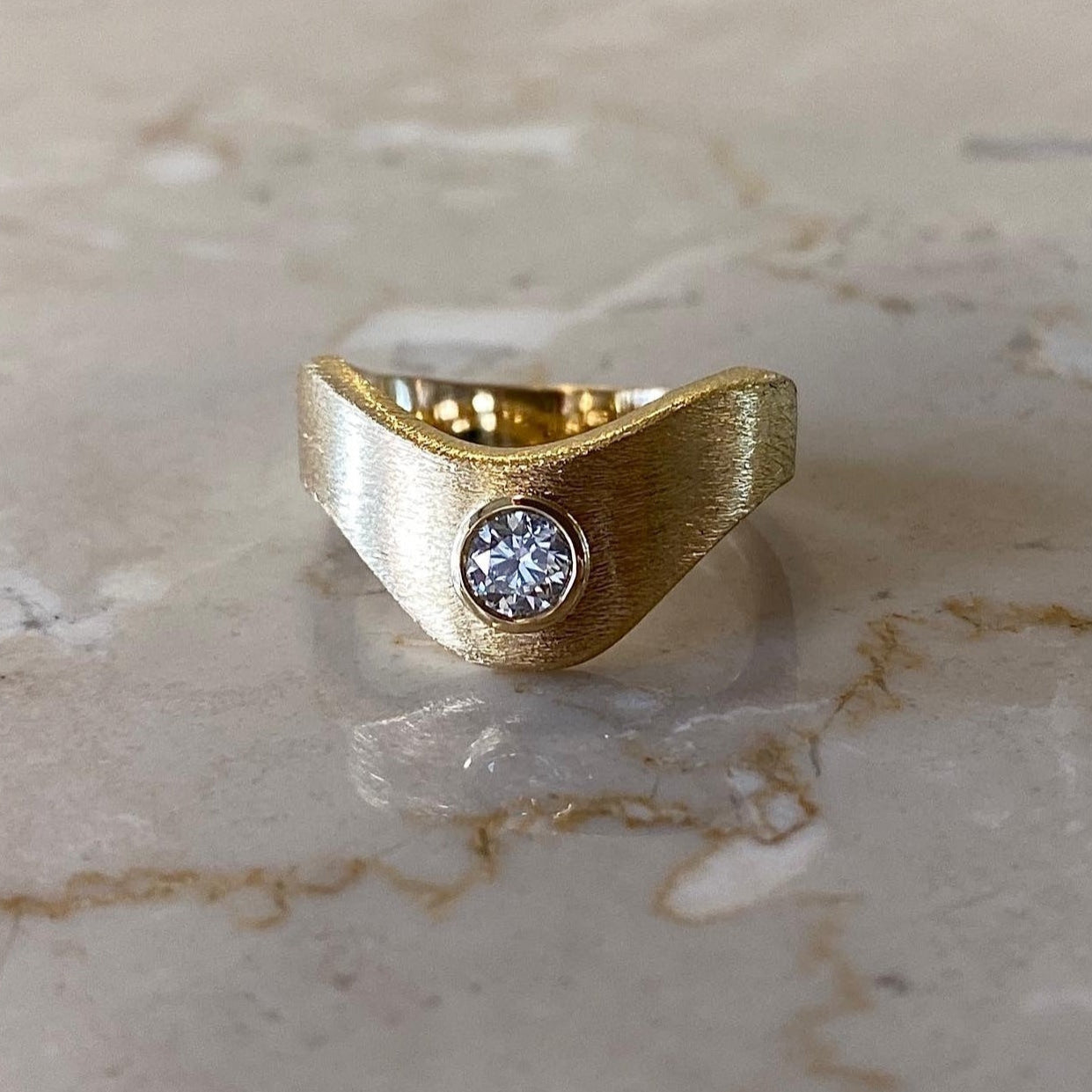 18 karat bred guldring i organisk bølgeform, ridset overflade, med stor 0,30ct hvid diamant.
